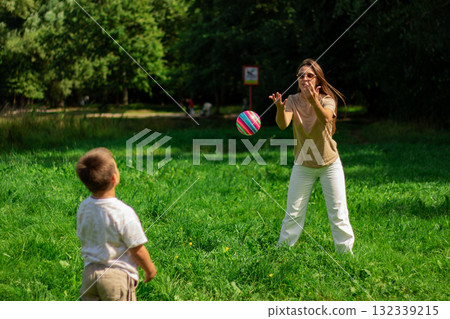 Mom and kid play ball together in nature during summer holidays. Playing ball with son in park. Catching ball. Mom and kid play ball together in nature during summer holidays. Playing ball with son in park. Catching ball. 132339215