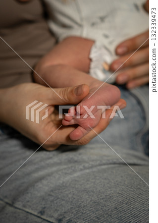 Mom gently holds her babys tiny foot while resting together in a cozy living room setting Mom gently holds her babys tiny foot while resting together in a cozy living room setting 132339473
