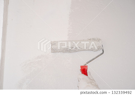A woman manually paints a wall with a paint roller. Painting the apartment A woman manually paints a wall with a paint roller. Painting the apartment 132339492