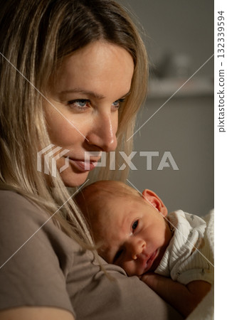Mom comforting baby in a cozy indoor setting during evening hours with soft lighting and a nurturing atmosphere Mom comforting baby in a cozy indoor setting during evening hours with soft lighting and a nurturing atmosphere 132339594