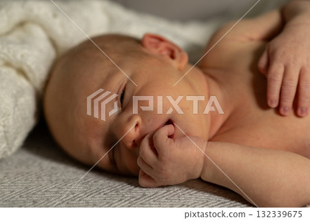 Baby lying on soft blanket, peacefully dreaming with fingers in mouth in warm indoor setting during morning light Baby lying on soft blanket, peacefully dreaming with fingers in mouth in warm indoor setting during morning light 132339675