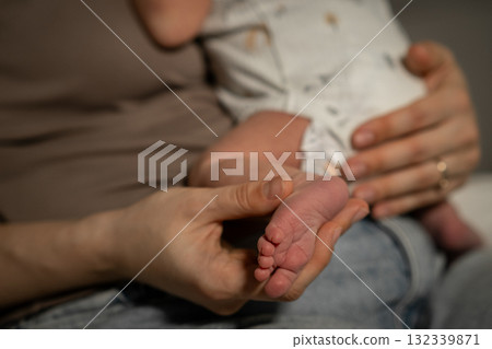 Mother cradling her baby, gently examining tiny foot in a cozy indoor setting during afternoon hours 132339871