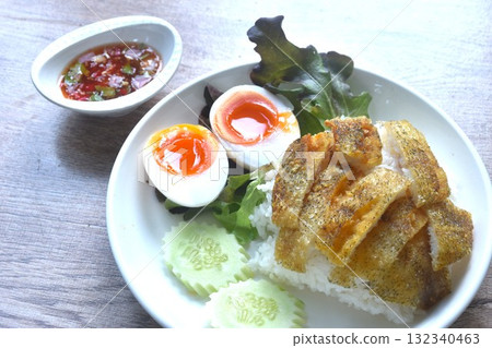 deep fried slice gourami fish topping plain rice with soft boiled egg and fresh vegetable on plate dipping spicy sweet fish sauce  132340463