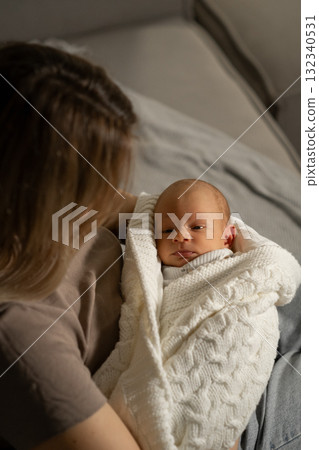 Mom gently holds her wrapped baby in a cozy indoor setting while sharing a quiet moment together during the early morning hours Mom gently holds her wrapped baby in a cozy indoor setting while sharing a quiet moment together during the early morning hours 132340531