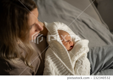 Mom cuddles newborn baby wrapped in cozy blanket during quiet evening at home, expressing love and connection in a serene atmosphere Mom cuddles newborn baby wrapped in cozy blanket during quiet evening at home, expressing love and connection in a serene atmosphere 132340532