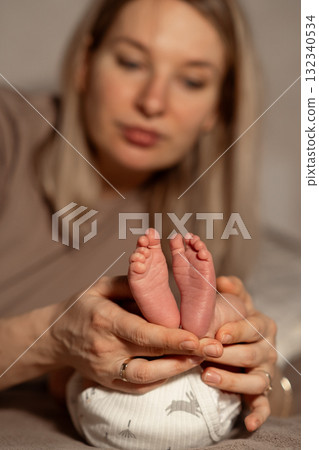 Mom gently holds her newborn babys tiny feet in a cozy indoor setting during a quiet moment of bonding in the afternoon light 132340534