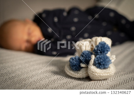 Cozy baby booties in focus while a sleeping infant rests peacefully in the background during a serene moment at home 132340627