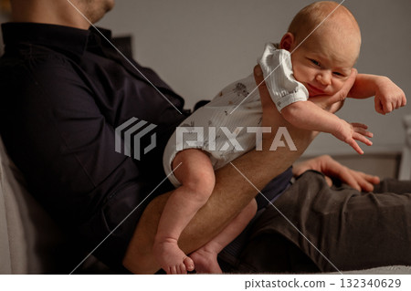 Baby happily playing on a parents leg while relaxing on a comfortable couch during a cozy indoor moment 132340629