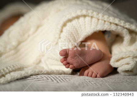Cozy baby feet peeking out from a knitted blanket during a quiet afternoon at home 132340943
