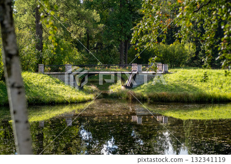 Bridge connecting serene waters and lush greenery near the Great Catherine Palace in Russia during a sunny day 132341119