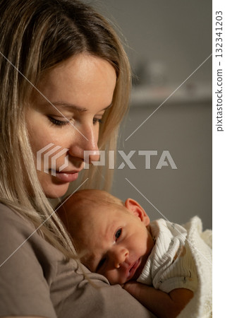 Mother gently cradles her newborn baby in a cozy indoor setting during the evening Mother gently cradles her newborn baby in a cozy indoor setting during the evening 132341203