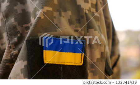 Close up of military blue-yellow chevron on shoulder of soldier at countryside. This emblem embodies the unbreakable spirit and pride of the ukrainian people. Concept of invasion resistance 132341439