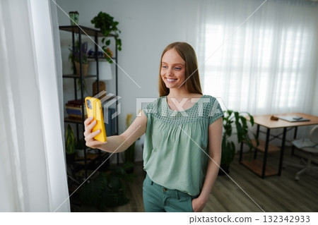 Smiling woman taking a selfie in a cozy, plant-filled room Smiling woman taking a selfie in a cozy, plant-filled room 132342933