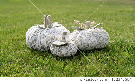 Trio of handmade lace pumpkins resting on bright green grass, rustic neutral tones and soft daylight create cozy garden mood 132343594