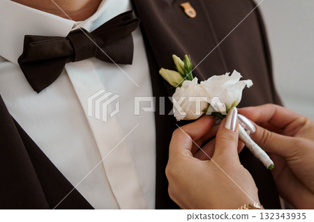 Elegant Groom Boutonniere Pinning: Brown Suit, White Flowers, Formal Wedding Attire, Close-up, Soft Lighting, Stylish Ceremony Detail. Elegant Groom Boutonniere Pinning: Brown Suit, White Flowers, Formal Wedding Attire, Close-up, Soft Lighting, Stylish Ceremony Detail. 132343935