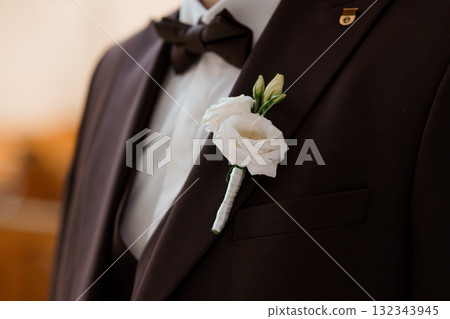 Elegant Groom's Boutonniere: Brown Suit, White Rose, Formal Wedding Attire, Close-up, Textured Lapel, Classic Style, Celebration, Sophisticated Detail. Elegant Groom's Boutonniere: Brown Suit, White Rose, Formal Wedding Attire, Close-up, Textured Lapel, Classic Style, Celebration, Sophisticated Detail. 132343945