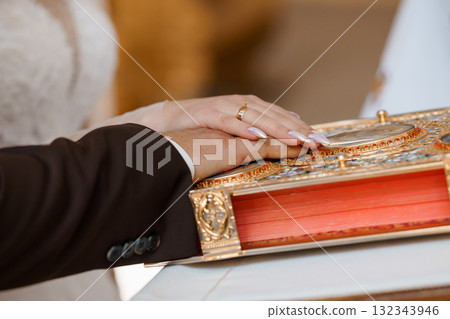 Wedding Ring Exchange Ceremony: Hands on Holy Book, Gold Band, Traditional Orthodox Symbolism, Close-Up, Warm Lighting, Brown and White Tones. Wedding Ring Exchange Ceremony: Hands on Holy Book, Gold Band, Traditional Orthodox Symbolism, Close-Up, Warm Lighting, Brown and White Tones. 132343946