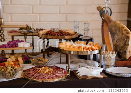 Gourmet Charcuterie Board Display with Prosciutto, Cheeses, Olives, and Large Ham Hock on Dark Table Setting. 132343953