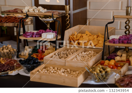 Gourmet Charcuterie Board Display with Variety of Cheeses, Meats, Nuts and Olives on Wooden Stands, Dark Background, Appetizer Table Setup. 132343954