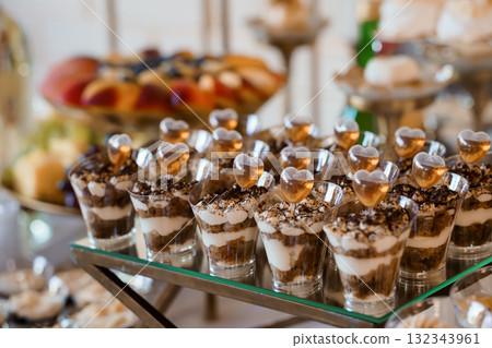 Elegant Wedding Dessert Display Featuring Chocolate Mousse Shooters with Heart-Shaped Garnishes on Silver Tiered Stand, Rich Brown and Gold Tones 132343961