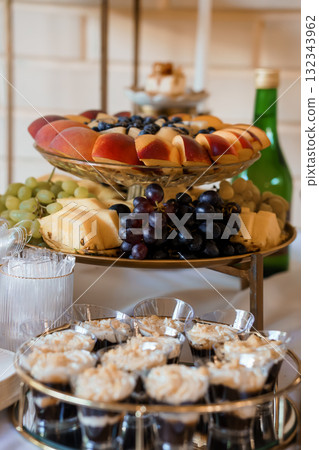 Elegant Dessert Spread Featuring Fresh Fruit, Mini Cheesecakes, and Wine on a Tiered Stand, Golden Accents, and Light Textures Elegant Dessert Spread Featuring Fresh Fruit, Mini Cheesecakes, and Wine on a Tiered Stand, Golden Accents, and Light Textures 132343962