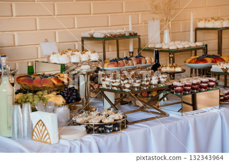 Elegant Dessert Buffet Display with Golden Stands, Fresh Fruit, Pastries and White Tablecloth Wedding Celebration, Gold Tones. 132343964