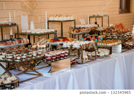 Luxurious Dessert Table Display at Wedding Reception with Gold Accents, White Linens, and Variety of Pastries. Luxurious Dessert Table Display at Wedding Reception with Gold Accents, White Linens, and Variety of Pastries. 132343965