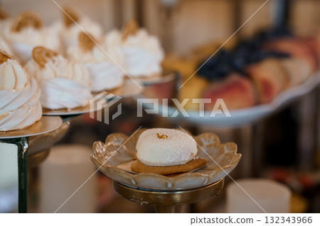 Elegant Dessert Display Featuring White Pavlovas with Gold Accents on Silver Platters, Wedding Cake Table, Soft Focus, Pastel Colors 132343966