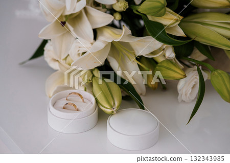 Wedding Rings with White Lilies Bouquet. Elegant Gold Bands, Floral Arrangement, Romance, Commitment, Soft Lighting, Celebration, Neutral Tones, Luxury. 132343985