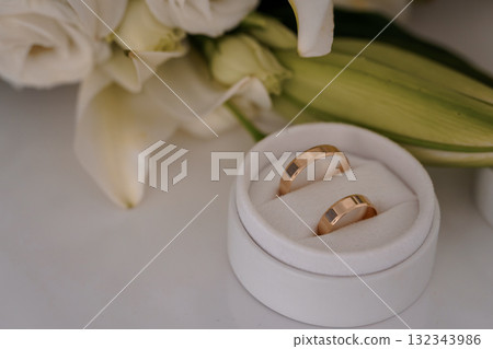 Romantic Wedding Rings Presentation with White Lilies. Rose Gold Bands, Symbolic Love, Celebration, Soft Focus, Elegant Floral Arrangement, Marriage Concept. Romantic Wedding Rings Presentation with White Lilies. Rose Gold Bands, Symbolic Love, Celebration, Soft Focus, Elegant Floral Arrangement, Marriage Concept. 132343986