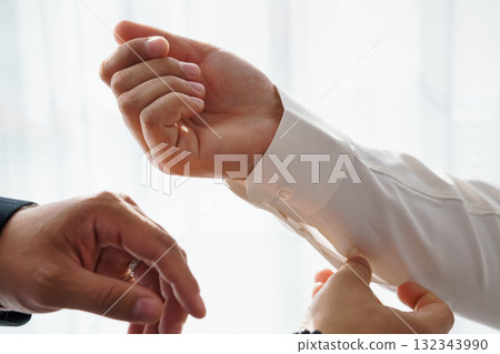 Formal Attire Assistance: Man Getting Cufflinks Fastened, White Shirt, Business Style, Close-Up, Warm Tones, Professional Grooming, Elegant Detail. Formal Attire Assistance: Man Getting Cufflinks Fastened, White Shirt, Business Style, Close-Up, Warm Tones, Professional Grooming, Elegant Detail. 132343990