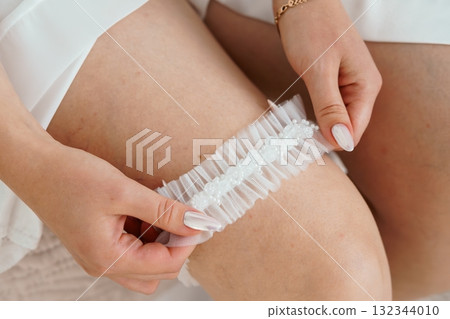 Bridal Garter Application: Close-Up of White Lace Legwear with Pearl Embellishments, Wedding Preparation, Delicate Texture, Soft Lighting. 132344010