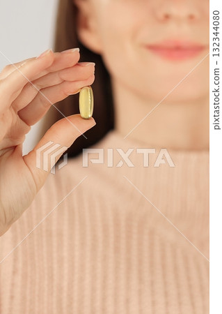Vertical close-up of an unrecognizable woman hollding a fish oil capsule, promoting daily supplement and heart health. Vertical close-up of an unrecognizable woman hollding a fish oil capsule, promoting daily supplement and heart health. 132344080