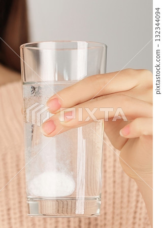 Vertical close-up of a hand holding a glass of water with a dissolving tablet inside. Concept of treatment, prevention and daily healthcare routine. Vertical close-up of a hand holding a glass of water with a dissolving tablet inside. Concept of treatment, prevention and daily healthcare routine. 132344094