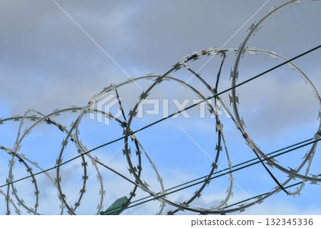 Barbed razor wire on a high-security building. Barbed wire and heavy wire fencing. Design of prisons, military facilities, nuclear power plants, and defense against illegal migration. 132345336