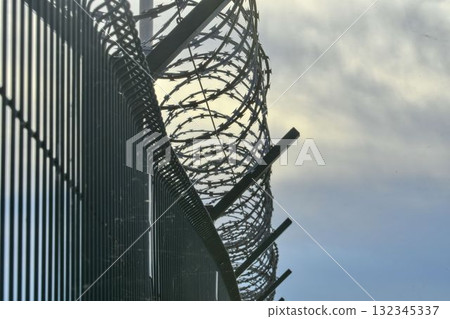 Razor barbed wire on a strictly guarded facility. Razor wire and durable wired fencing. Concept for prisons, military facilities, and nuclear power plants. 132345337