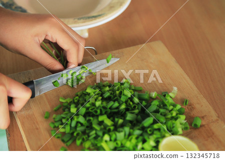 hands cutting green spring onion on cutting board for cooking 132345718