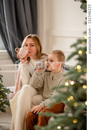 Mother and Child Enjoying Hot Drinks by Christmas Tree 132346225