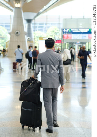Business traveler walking through a modern airport terminal with rolling luggage in hand during a busy afternoon 132346782