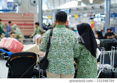 Travelers in matching green outfits prepare for departure at the airport with luggage and family in the background during peak travel hours 132346784