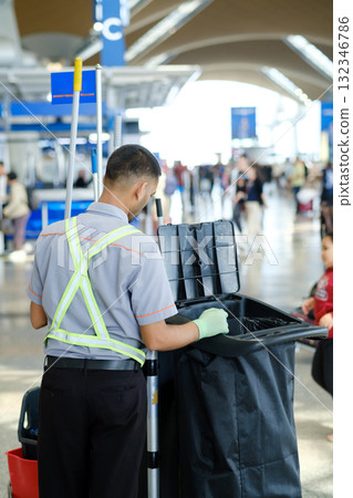 Waste management worker cleans terminal area in busy airport setting during daylight hours Waste management worker cleans terminal area in busy airport setting during daylight hours 132346786