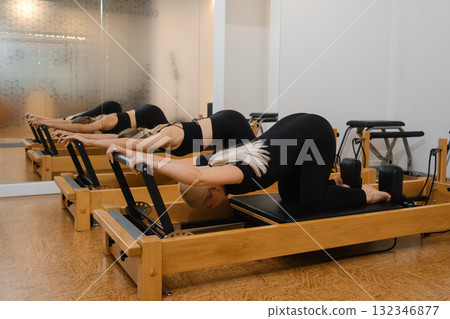 Group of women practicing pilates on reformers in a bright studio environment during a fitness class session in the afternoon Group of women practicing pilates on reformers in a bright studio environment during a fitness class session in the afternoon 132346877