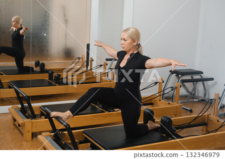 Woman practicing on a reformer machine in a bright studio during a pilates class focused on improving flexibility and strength 132346979