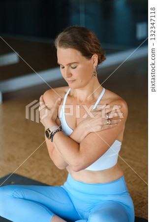 Yoga practitioner performs a relaxing seated pose in a spacious and well-lit studio during an early morning session focused on mindfulness and self-care 132347118