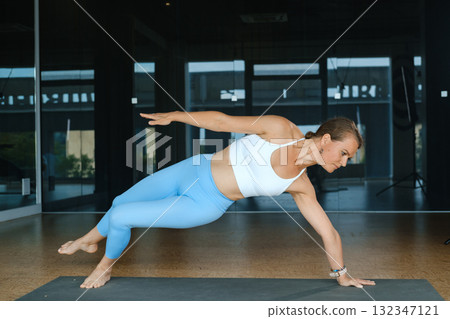 Dynamic yoga practice showcasing a woman performing an advanced balance pose in a bright studio setting during daylight hours Dynamic yoga practice showcasing a woman performing an advanced balance pose in a bright studio setting during daylight hours 132347121