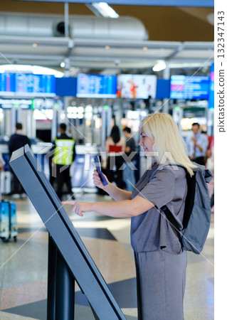 Traveler uses self-check-in kiosk at busy airport while preparing for upcoming flight to an international destination Traveler uses self-check-in kiosk at busy airport while preparing for upcoming flight to an international destination 132347143