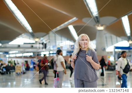 Woman standing in a busy international airport terminal with people walking around and modern architecture in the background during daytime travel hours 132347148