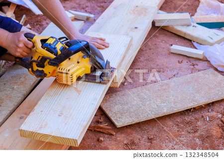Carpenter expertly cuts long wooden planks with circular saw while working at construction site 132348504