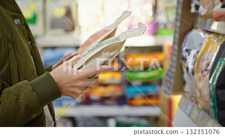 A woman comparing two packages of dry pet food in a store, holding them in her hands and deciding which one to buy. Consumer choice, healthy nutrition and responsible pet owner in retail environment. A woman comparing two packages of dry pet food in a store, holding them in her hands and deciding which one to buy. Consumer choice, healthy nutrition and responsible pet owner in retail environment. 132351076