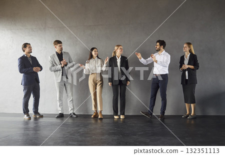 Business people in formal clothes talking indoors standing in a row on dark gray wall background. 132351113